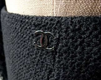Closeup of the 2003 vintage classic Chanel black boucle wool suit, the jacket and skirt both edged with a looped wool, the jacket closes at the neck with a black camellia flower button; jacket size 42 and skirt size 40.