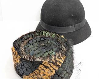 A vintage black velvet pillbox hat with a black green and gold feather trim and a black net veil, label inside reads LaVerne; along with a black wool felt cloche hat with a ribbon band