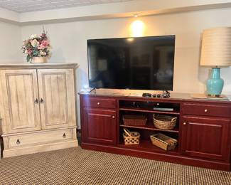 Large wood media console, flat-screen TV, a teal ceramic lamp, and a distressed wood armoire