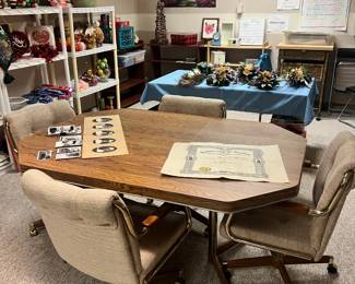 Octagonal wood-grain laminate table with four upholstered brass-frame chairs on rolling casters