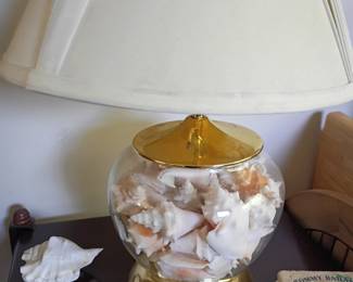 Glass lamp filled with seashells, brass base and white shade