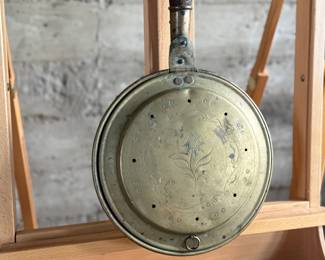 Brass bed warmer with floral etching and decorative perforations on the lid. The piece features a wooden turned handle with a rich patina and a hinged lid. The brass showcases signs of use with wear and age-related patina. The perforations were traditionally used for dispersing heat by placing warm materials inside the bed warmer. Suitable for collectors or historical display.