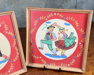 Two framed prints by Art of California, measuring 10.75” H x 10.75” W each. These are handcrafted reproductions of original paintings by Viennese artist Friedl, showcasing charming dance scenes with bright red backgrounds and decorative floral borders. Each piece is framed in light wood and features a paper backing with labeled production details.