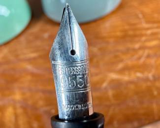 Esterbrook dip pens featuring metal nibs marked ‘Esterbrook 9556’ with black and green handles. Each pen is paired with a ceramic holder in complementing colors: green and blue-gray. Both pens are marked ‘Esterbrook Made in U.S.A.’ on the handles, denoting their authenticity. Well-preserved and functional writing tools, ideal for collectors or calligraphy enthusiasts.