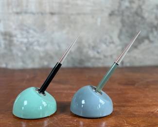 Esterbrook dip pens featuring metal nibs marked ‘Esterbrook 9556’ with black and green handles. Each pen is paired with a ceramic holder in complementing colors: green and blue-gray. Both pens are marked ‘Esterbrook Made in U.S.A.’ on the handles, denoting their authenticity. Well-preserved and functional writing tools, ideal for collectors or calligraphy enthusiasts.