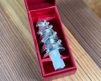 Silver-toned wine stopper adorned with intricate detailing, presented in its original Neiman Marcus red box. The stopper features a decorative design and includes a rubberized insert for a secure fit. Box measures approximately 4 inches in length. Appears to be in excellent condition with minimal wear on the packaging.