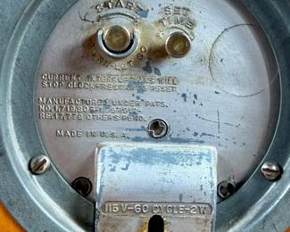 Vintage Chronomaster electric clock featuring a wood housing with black base and decorative brass-tone accents. The clock measures 9” in height and includes an electrical cord for operation. The back panel displays the manufacturer’s details, marked ‘Made in U.S.A.’ and specifications for 115V-60 cycle-2W. Tested and in working condition.