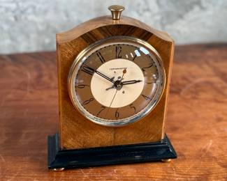 Vintage Chronomaster electric clock featuring a wood housing with black base and decorative brass-tone accents. The clock measures 9” in height and includes an electrical cord for operation. The back panel displays the manufacturer’s details, marked ‘Made in U.S.A.’ and specifications for 115V-60 cycle-2W. Tested and in working condition.