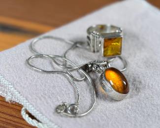This lot features a stunning ring and necklace made from sterling silver and featuring amber center stones. The ring comes in a size 7 and the chain measures, 17”. Both items have a total approx. weight of 25.00 grams.