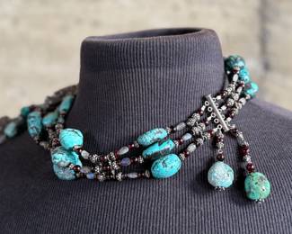 Sterling silver statement necklace featuring an intricate design with various gemstones. The hallmark ‘925’ is stamped on the reverse side, affirming its sterling silver composition. The piece includes multiple strands and pendants accented with gemstones. In good condition and designed with a secure clasp for wearability. This necklace measures, 18” with a total approx. weight of 356.22 grams.