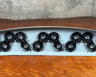 Vintage 1978 Star Wars action figure display stand by GMFGI. Marked ‘321E 001’ with a copyright of ‘G.M.F.G.I. – 1978’. Features slots marked with character names including Stormtrooper, Darth Vader, Luke Skywalker, and Princess Leia. Made of gray plastic with attached gear mechanisms on the back and visible character labels on the front. Some wear consistent with age.