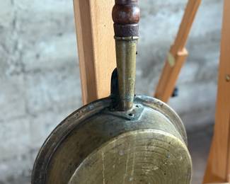 Brass bed warmer with floral etching and decorative perforations on the lid. The piece features a wooden turned handle with a rich patina and a hinged lid. The brass showcases signs of use with wear and age-related patina. The perforations were traditionally used for dispersing heat by placing warm materials inside the bed warmer. Suitable for collectors or historical display.