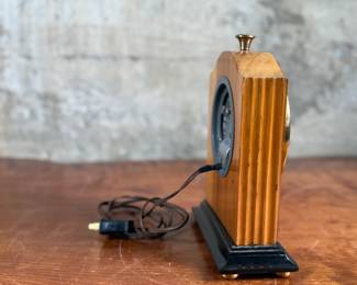 Vintage Chronomaster electric clock featuring a wood housing with black base and decorative brass-tone accents. The clock measures 9” in height and includes an electrical cord for operation. The back panel displays the manufacturer’s details, marked ‘Made in U.S.A.’ and specifications for 115V-60 cycle-2W. Tested and in working condition.