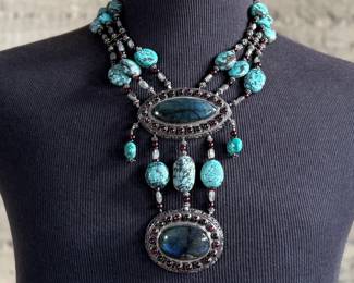 Sterling silver statement necklace featuring an intricate design with various gemstones. The hallmark ‘925’ is stamped on the reverse side, affirming its sterling silver composition. The piece includes multiple strands and pendants accented with gemstones. In good condition and designed with a secure clasp for wearability. This necklace measures, 18” with a total approx. weight of 356.22 grams.