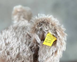 Steiff mohair teddy bear featuring a soft brown mohair exterior and traditional button-in-ear yellow tag. Adorned with a red bow around the neck, this bear’s label indicates it is made of 53% wool and 47% cotton. Includes an “Original Teddybar” tag and is in great collectible condition.