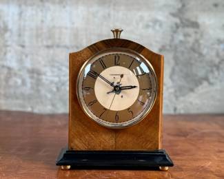 Vintage Chronomaster electric clock featuring a wood housing with black base and decorative brass-tone accents. The clock measures 9” in height and includes an electrical cord for operation. The back panel displays the manufacturer’s details, marked ‘Made in U.S.A.’ and specifications for 115V-60 cycle-2W. Tested and in working condition.