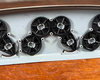 Vintage 1978 Star Wars action figure display stand by GMFGI. Marked ‘321E 001’ with a copyright of ‘G.M.F.G.I. – 1978’. Features slots marked with character names including Stormtrooper, Darth Vader, Luke Skywalker, and Princess Leia. Made of gray plastic with attached gear mechanisms on the back and visible character labels on the front. Some wear consistent with age.