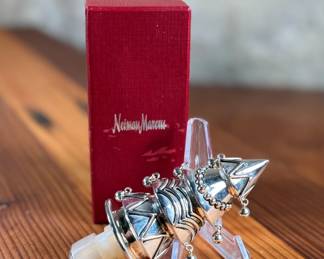 Silver-toned wine stopper adorned with intricate detailing, presented in its original Neiman Marcus red box. The stopper features a decorative design and includes a rubberized insert for a secure fit. Box measures approximately 4 inches in length. Appears to be in excellent condition with minimal wear on the packaging.