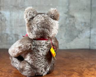 Steiff mohair teddy bear featuring a soft brown mohair exterior and traditional button-in-ear yellow tag. Adorned with a red bow around the neck, this bear’s label indicates it is made of 53% wool and 47% cotton. Includes an “Original Teddybar” tag and is in great collectible condition.