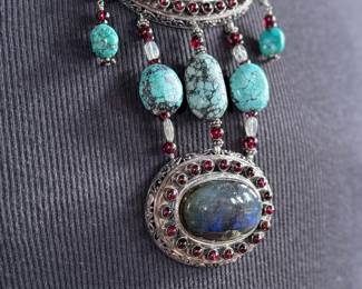 Sterling silver statement necklace featuring an intricate design with various gemstones. The hallmark ‘925’ is stamped on the reverse side, affirming its sterling silver composition. The piece includes multiple strands and pendants accented with gemstones. In good condition and designed with a secure clasp for wearability. This necklace measures, 18” with a total approx. weight of 356.22 grams.