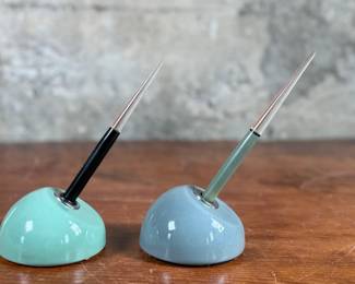 Esterbrook dip pens featuring metal nibs marked ‘Esterbrook 9556’ with black and green handles. Each pen is paired with a ceramic holder in complementing colors: green and blue-gray. Both pens are marked ‘Esterbrook Made in U.S.A.’ on the handles, denoting their authenticity. Well-preserved and functional writing tools, ideal for collectors or calligraphy enthusiasts.