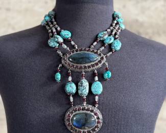 Sterling silver statement necklace featuring an intricate design with various gemstones. The hallmark ‘925’ is stamped on the reverse side, affirming its sterling silver composition. The piece includes multiple strands and pendants accented with gemstones. In good condition and designed with a secure clasp for wearability. This necklace measures, 18” with a total approx. weight of 356.22 grams.