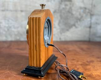 Vintage Chronomaster electric clock featuring a wood housing with black base and decorative brass-tone accents. The clock measures 9” in height and includes an electrical cord for operation. The back panel displays the manufacturer’s details, marked ‘Made in U.S.A.’ and specifications for 115V-60 cycle-2W. Tested and in working condition.