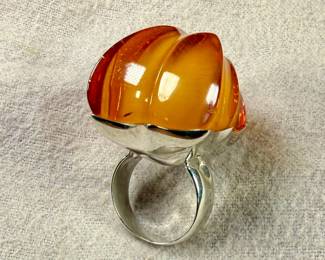 Sterling silver ring featuring a large, polished amber cabochon centerpiece with organic and irregular contours. The amber showcases rich honey tones with natural inclusions visible within. The mounting is made from solid sterling silver and complements the amber’s unique shape. Coin shown for size reference. Comes in a size 9 with a total approx. weight of 27.21 grams.