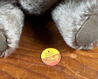 Steiff mohair teddy bear featuring a soft brown mohair exterior and traditional button-in-ear yellow tag. Adorned with a red bow around the neck, this bear’s label indicates it is made of 53% wool and 47% cotton. Includes an “Original Teddybar” tag and is in great collectible condition.