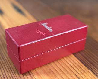 Silver-toned wine stopper adorned with intricate detailing, presented in its original Neiman Marcus red box. The stopper features a decorative design and includes a rubberized insert for a secure fit. Box measures approximately 4 inches in length. Appears to be in excellent condition with minimal wear on the packaging.