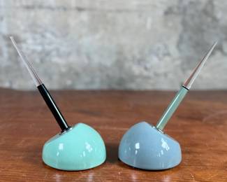 Esterbrook dip pens featuring metal nibs marked ‘Esterbrook 9556’ with black and green handles. Each pen is paired with a ceramic holder in complementing colors: green and blue-gray. Both pens are marked ‘Esterbrook Made in U.S.A.’ on the handles, denoting their authenticity. Well-preserved and functional writing tools, ideal for collectors or calligraphy enthusiasts.