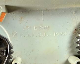 Vintage 1978 Star Wars action figure display stand by GMFGI. Marked ‘321E 001’ with a copyright of ‘G.M.F.G.I. – 1978’. Features slots marked with character names including Stormtrooper, Darth Vader, Luke Skywalker, and Princess Leia. Made of gray plastic with attached gear mechanisms on the back and visible character labels on the front. Some wear consistent with age.