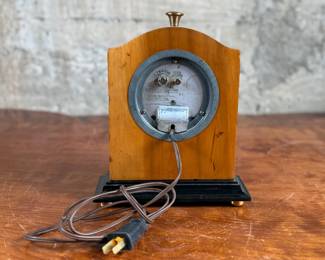 Vintage Chronomaster electric clock featuring a wood housing with black base and decorative brass-tone accents. The clock measures 9” in height and includes an electrical cord for operation. The back panel displays the manufacturer’s details, marked ‘Made in U.S.A.’ and specifications for 115V-60 cycle-2W. Tested and in working condition.