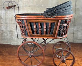 This lot features a beautiful antique Victorian-style doll carriage made from wicker, wood, and metal. This piece measures, 17.5” H x 19” W x 7” D.