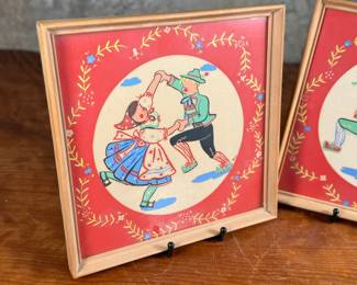 Two framed prints by Art of California, measuring 10.75” H x 10.75” W each. These are handcrafted reproductions of original paintings by Viennese artist Friedl, showcasing charming dance scenes with bright red backgrounds and decorative floral borders. Each piece is framed in light wood and features a paper backing with labeled production details.