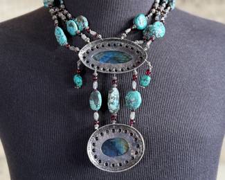 Sterling silver statement necklace featuring an intricate design with various gemstones. The hallmark ‘925’ is stamped on the reverse side, affirming its sterling silver composition. The piece includes multiple strands and pendants accented with gemstones. In good condition and designed with a secure clasp for wearability. This necklace measures, 18” with a total approx. weight of 356.22 grams.