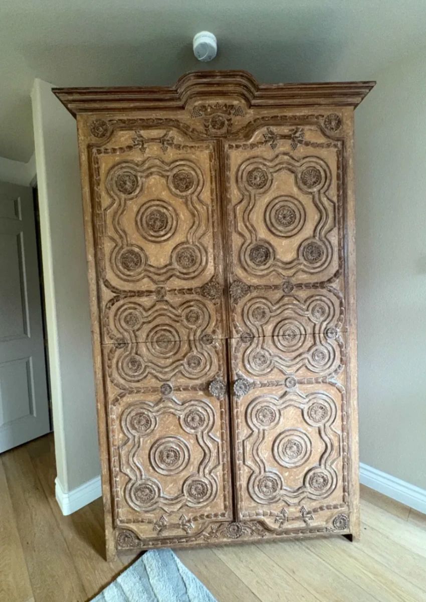 Hand-Carved Armoire / Entertainment Cabinet Exceptional two-door armoire featuring intricate hand-carved rosette and cartouche panels across every door panel, with a beautifully detailed broken pediment crown. Spanish/Mexican colonial style with a warm distressed finish. Interior is fitted with shelving — ideal for use as an entertainment cabinet, wardrobe, or display piece. This piece was originally several thousand dollars and the craftsmanship shows. A true statement piece and one of the standout items in this sale. Please note: TV is not included.