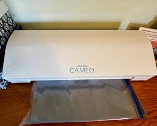Silhouette Cameo electronic cutting machine that connects to a computer or other device. It can cut through a variety of materials such as paper, cardstock, vinyl, and fabric up to 12" wide!