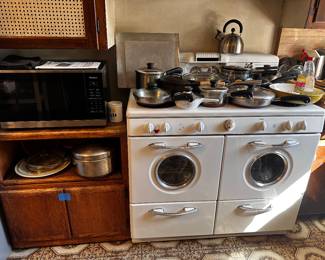 Panasonic microwave with paperwork on a stand that needs TLC and pots and pans mostly stainless Revere Ware