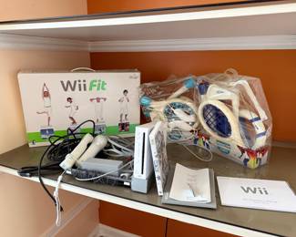 Nintendo Wii console (white) Wii Fit box Wii Sports game case (appears to be “Wii Sports”/“Wii Play” style case next to console) Two Wii Remotes (white) Nunchuk controller(s) attached to cables Sensor bar Power adapter and AV cables Two plastic accessory packs (sports pack with tennis rackets, golf club, baseball bat attachments, etc.) in clear bags Wii Operations Manual booklet Additional small instruction booklet BUY IT ALL TODAY $150
