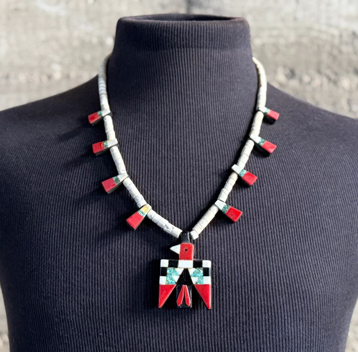 This lot features an antique Santo Domingo Pueblo (Kewa) Thunderbird necklace, an iconic style frequently made during the Depression era using repurposed materials like plastic from battery casings, phonograph records, and turquoise. This necklace has mosaic inlay typically utilizing turquoise, coral, and black jet (often repurposed plastic). These necklaces are highly collectible examples of Southwestern cultural heritage and resourcefulness. Handcrafted by artists from the Kewa (Santo Domingo) Pueblo, with many historic examples dating back to the 1920s–1940s. Measures, 22”.