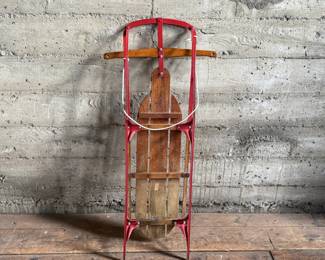 Wooden Flexible Flyer Yankee Clipper sled featuring steel runners painted in red and a wooden deck with printed branding. The sled includes a wooden crossbar for steering and a rope control. Signs of wear consistent with age and use, including scratches and minor rust on metal parts, are visible. A classic item for collectors or enthusiasts of vintage winter gear. Measures, 44” H x 20.5” W.