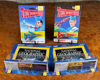 Two Matchbox Thunderbirds action figures (Scott Tracy and Alan Tracy) on original carded packaging, and two Micro Machines National Geographic Collections: #3 Moon Explorers and #4 Space Pioneers. All items are in original unopened packaging with visible wear consistent with age. Educational and collectible sets representing iconic figures and space exploration themes.