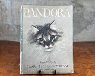 First edition of ‘Pandora, ‘ written and illustrated by Clare Turlay Newberry, published by Harper & Brothers. The book showcases charming illustrations and a story centered around a cat. It features a worn illustrated hardcover with signs of age-related wear, including scuffs and edge fraying. The interior remains intact with detailed illustrations and text reflective of Newberry’s style.