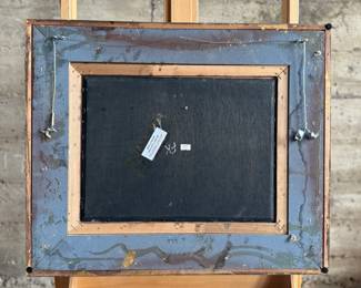 Framed oil on panel painting depicting a detailed village scene with several figures and buildings. Signed by the artist in the lower right corner. Encased in an ornate, gilt wooden frame with floral details. Measures in frame, 20.75” H x 24.75” W.