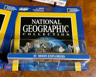 Two Matchbox Thunderbirds action figures (Scott Tracy and Alan Tracy) on original carded packaging, and two Micro Machines National Geographic Collections: #3 Moon Explorers and #4 Space Pioneers. All items are in original unopened packaging with visible wear consistent with age. Educational and collectible sets representing iconic figures and space exploration themes.