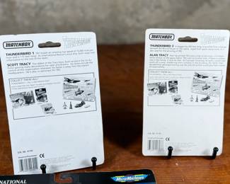 Two Matchbox Thunderbirds action figures (Scott Tracy and Alan Tracy) on original carded packaging, and two Micro Machines National Geographic Collections: #3 Moon Explorers and #4 Space Pioneers. All items are in original unopened packaging with visible wear consistent with age. Educational and collectible sets representing iconic figures and space exploration themes.