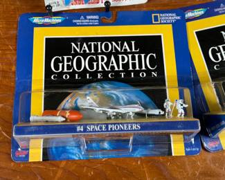 Two Matchbox Thunderbirds action figures (Scott Tracy and Alan Tracy) on original carded packaging, and two Micro Machines National Geographic Collections: #3 Moon Explorers and #4 Space Pioneers. All items are in original unopened packaging with visible wear consistent with age. Educational and collectible sets representing iconic figures and space exploration themes.