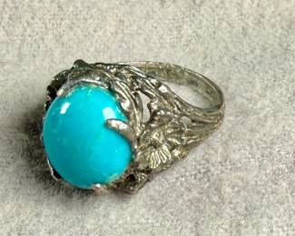 Sterling silver ring featuring a vibrant turquoise cabochon centerpiece. The band is ornately designed with detailed organic elements resembling leaves or vines. The turquoise stone is prominently set, securely held by prongs. The interior of the band shows slight wear, consistent with age and previous use. Comes in a size 6.