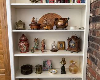 Bookshelf full of collectibles including Borghese book ends, antique pocket watch, German music boxes, Fenton glass